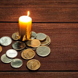 Mit Stable Diffusion erzeugtes Foto der Oberfläche eines einfachen Holztisches, auf dem eine Kerze steht, um die herum einige Münzen liegen.