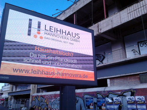 Ströer-Werbetafel an der Spinnereistraße in Hannover-Linden, im Hintergrund die zerfallende Baussubstanz der monströsen Ruine des Ihmezentrums. Text auf der Werbetafel: Leihhaus Hannovera GmbH -- Das Original seit 1948 -- Haushaltsloch? -- Da hilft ein Pfandkredit schnell und unbürokratisch! -- www.leihhaus-hannovera.de